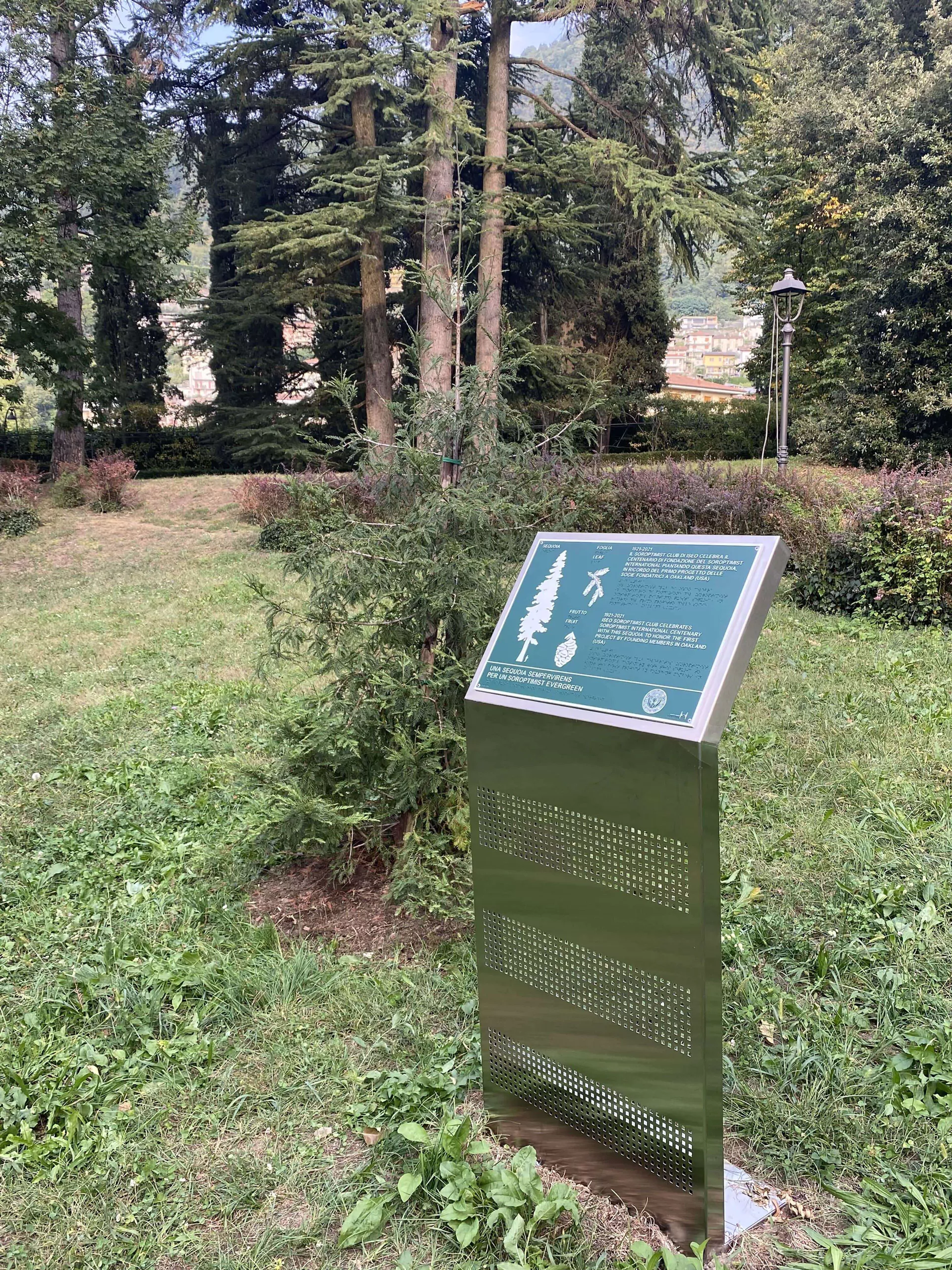 Pisogne, Parco Comunale. Il pannello tattile con disegni e scritte in bianco su fondo verde consente di esplorare la forma dell’esemplare adulto di una Sequoia rispetto alla figura umana, le foglie e il frutto. Si può leggere in Braille la motivazione celebrativa del Soroptimist International.